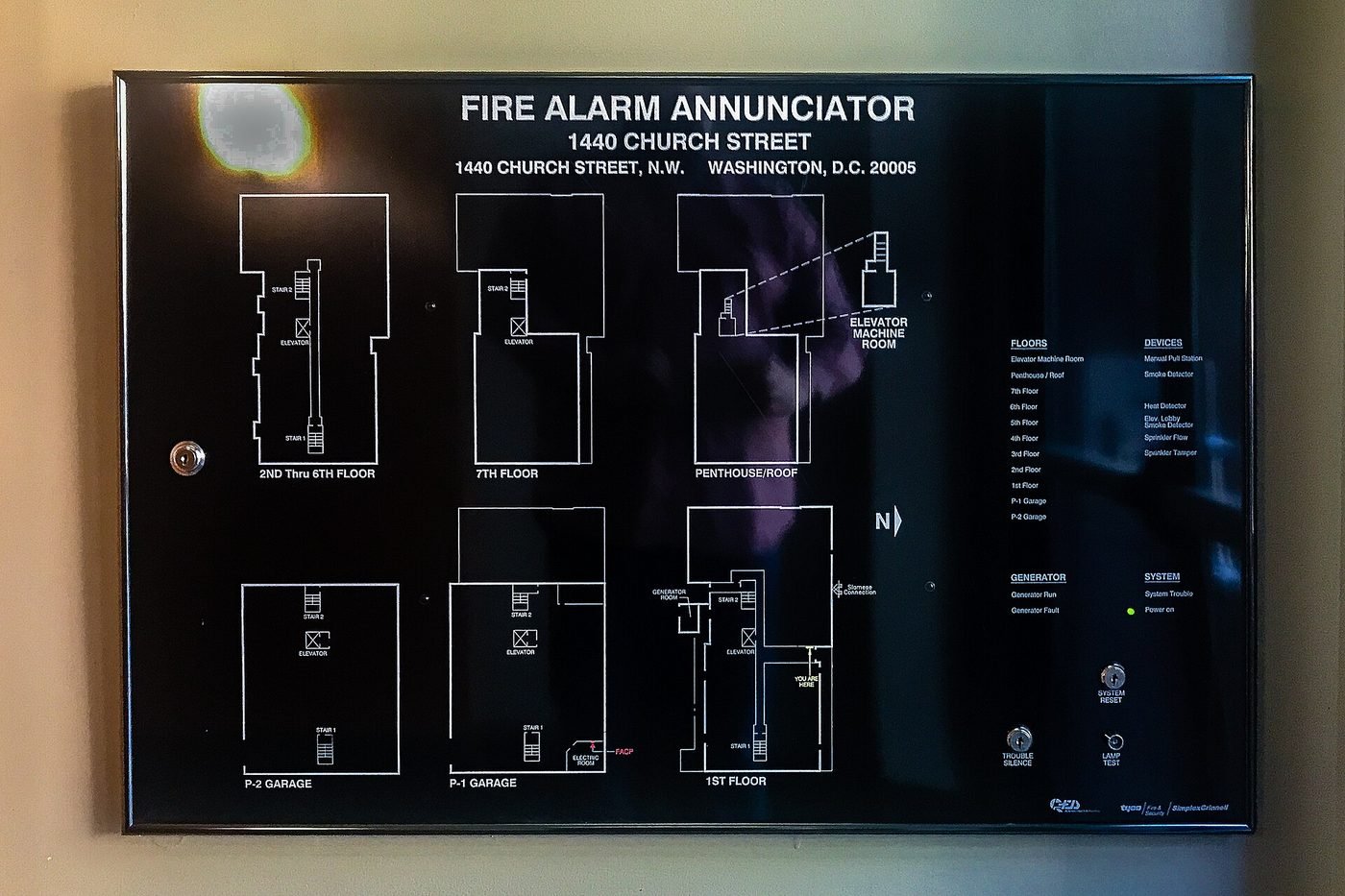 Fire alarm annunciator panel mounted in a commercial building lobby showing floor-by-floor zone plans and device legends for smoke detectors, heat detectors, sprinkler flow and manual pull stations