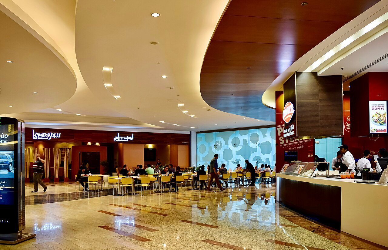 Fit-out snagging Dubai - completed commercial interior at Al Ghurair Centre showing curved gypsum bulkheads, cove lighting, tenant shopfronts and polished stone flooring