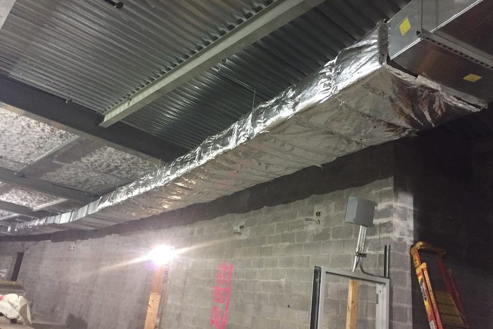 Duct insulation being applied to HVAC ductwork during fit-out, the point after which test holes and access panels can no longer be added without cutting the insulation open