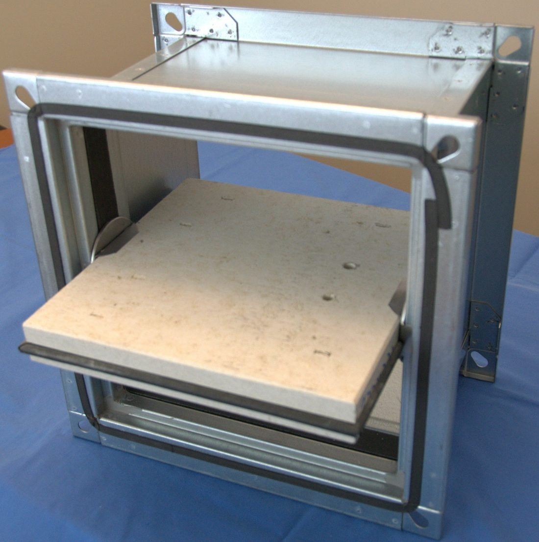 A 90 minute rated fire damper unit for a 30 by 30 centimetre duct, shown opened to reveal the internal blade assembly and fusible link mechanism that closes the damper on heat detection