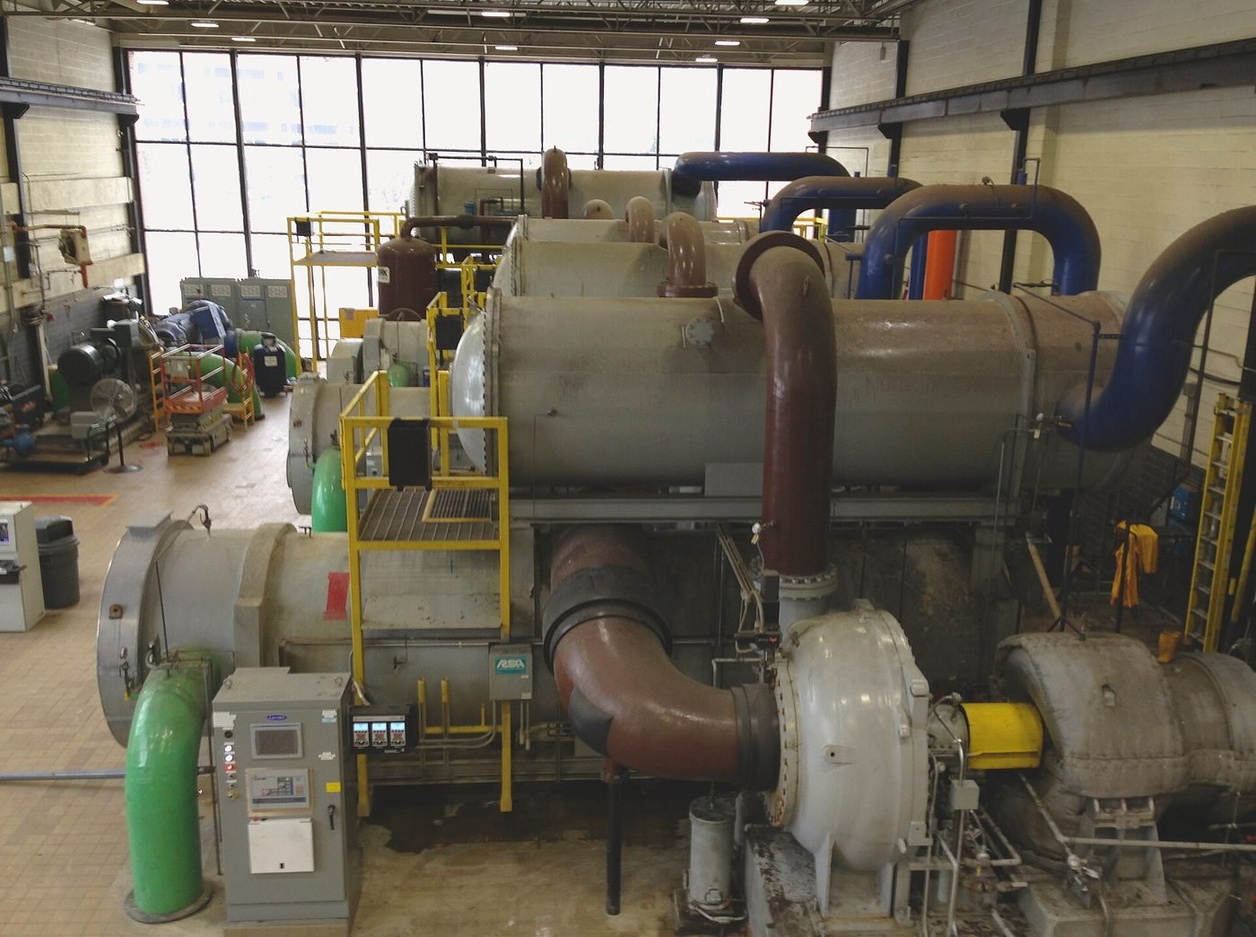 Large centrifugal chillers installed in a district cooling plant room, showing the compressor sets, chilled water headers and insulated pipework that supply cooling to connected buildings