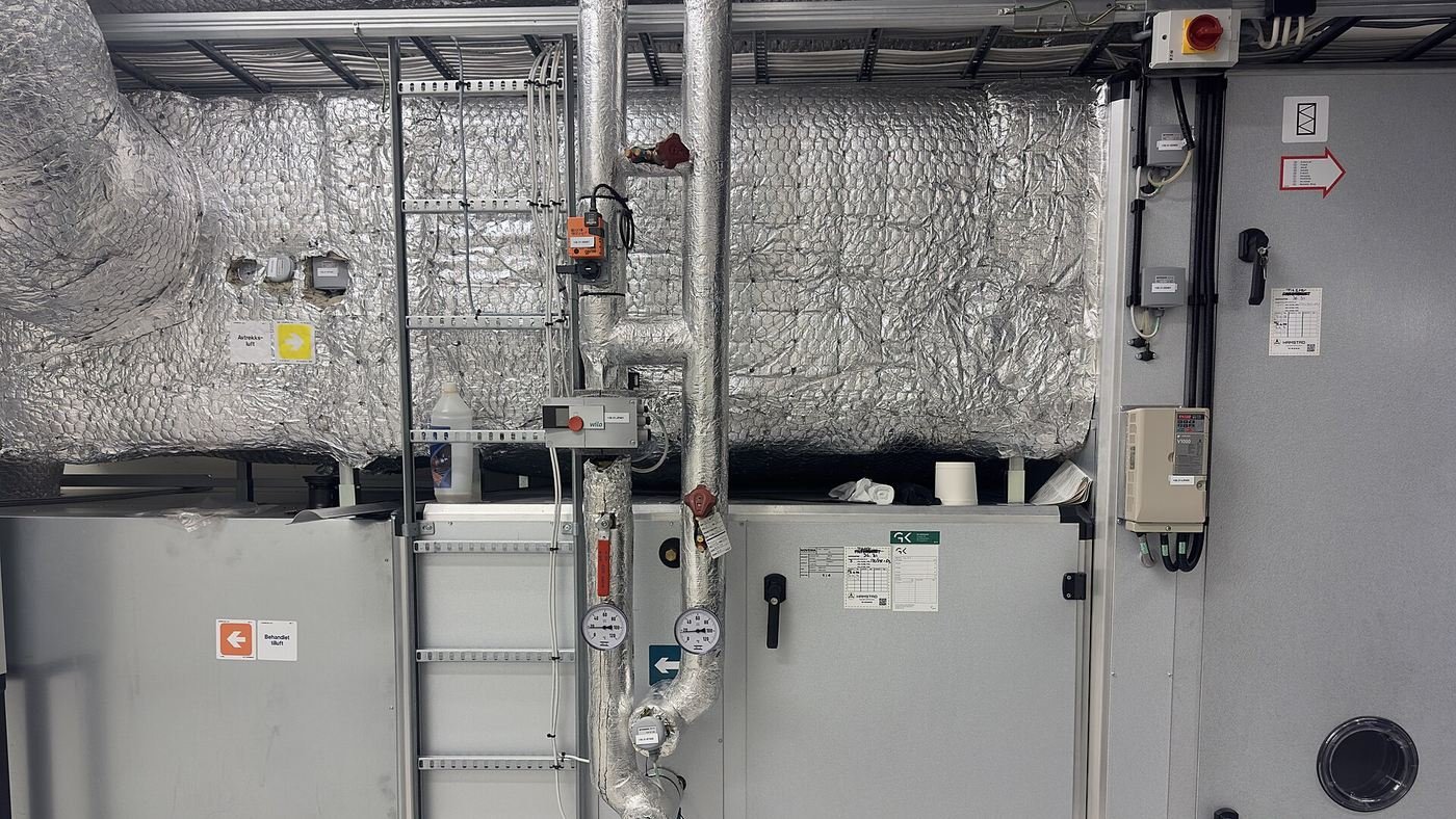 MEP coordination fit out services in a plant room: insulated ventilation ductwork, chilled water flow and return pipework with isolation valves and gauges, cable containment and an electrical control panel routed within a constrained ceiling void